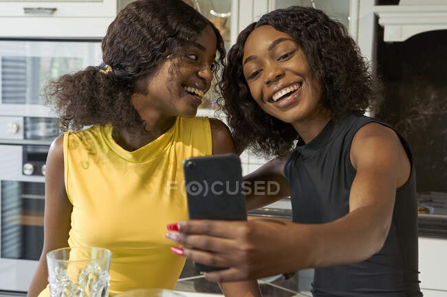 Портрет двох щасливих друзів, які беруть селфі зі смартфоном на кухні — стокове фото
