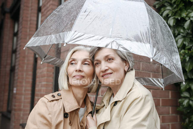 Sonrientes amigas bajo paraguas en un día lluvioso - foto de stock