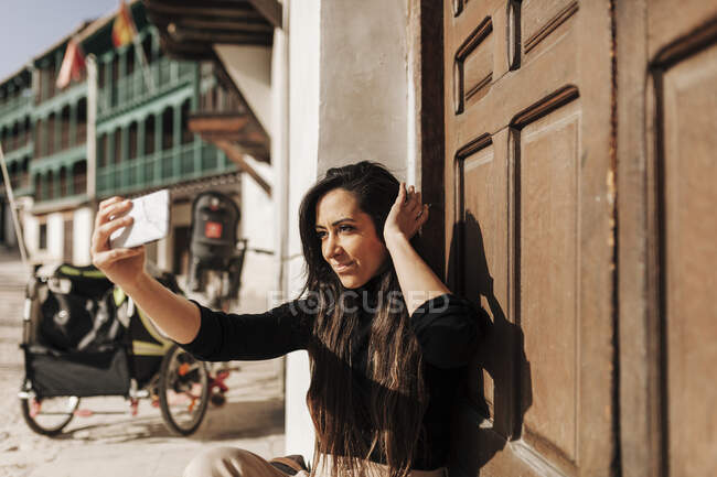 Sorrindo mulher tomando selfie enquanto sentado à porta — Fotografia de Stock