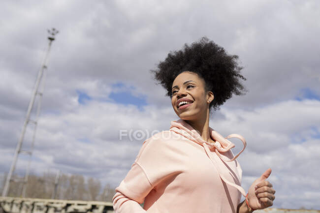 Mujer sonriente con camisa encapuchada mirando hacia otro lado durante el día soleado - foto de stock