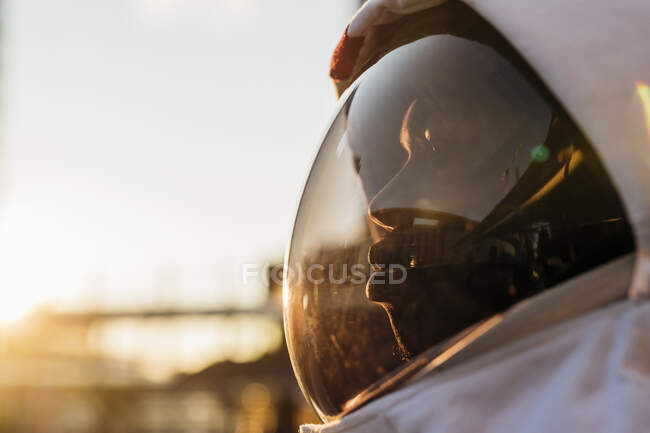 Mid adult astronaut wearing space helmet looking away during sunset - foto de stock