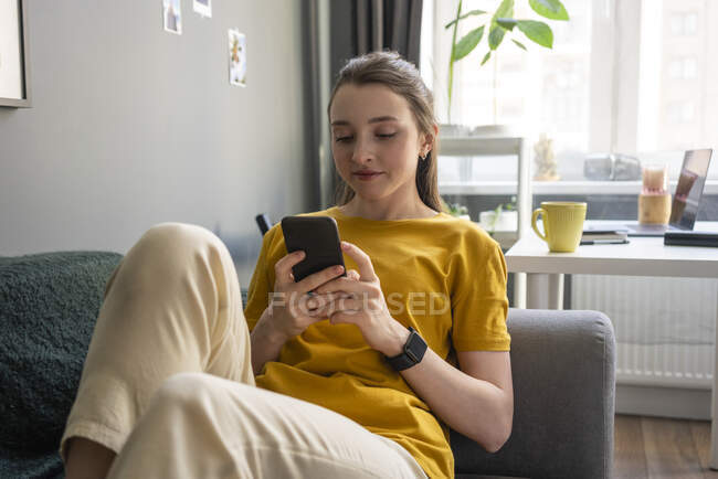 Mujer usando el teléfono inteligente mientras está sentado en el sofá - foto de stock