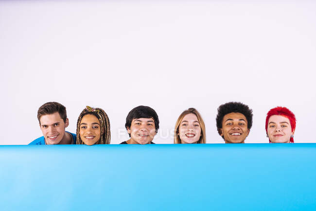 Sonrientes amigos multi-étnicos hombres y mujeres detrás de telón de fondo azul - foto de stock