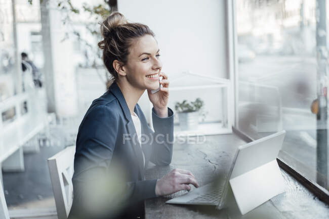 Female entrepreneur with digital tablet talking on mobile phone at cafe — Stock Photo