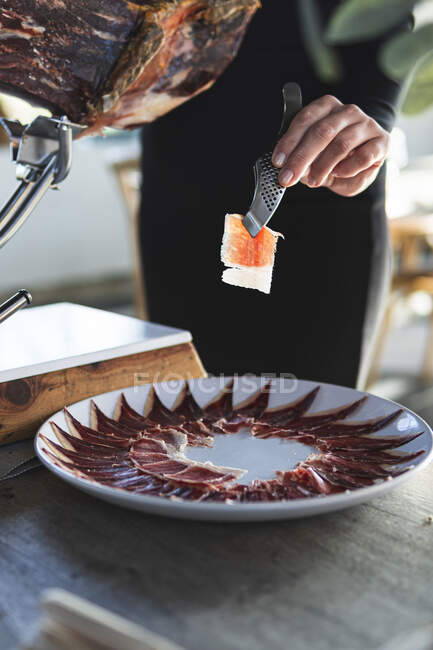 Жіночий шеф-кухар розміщує скибочки шинки на столі в ресторані — стокове фото