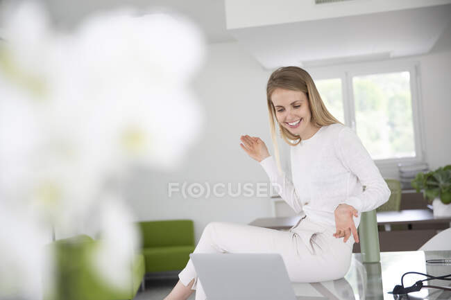 Feliz mujer de negocios gesto mientras está sentado en el escritorio durante la videoconferencia a través de la computadora portátil en la oficina - foto de stock