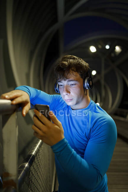 Atleta usando telefone enquanto está de pé por trilhos — Fotografia de Stock