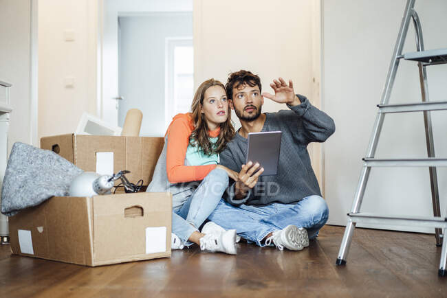 Young couple sitting with digital tablet discussing at new home — Stock Photo