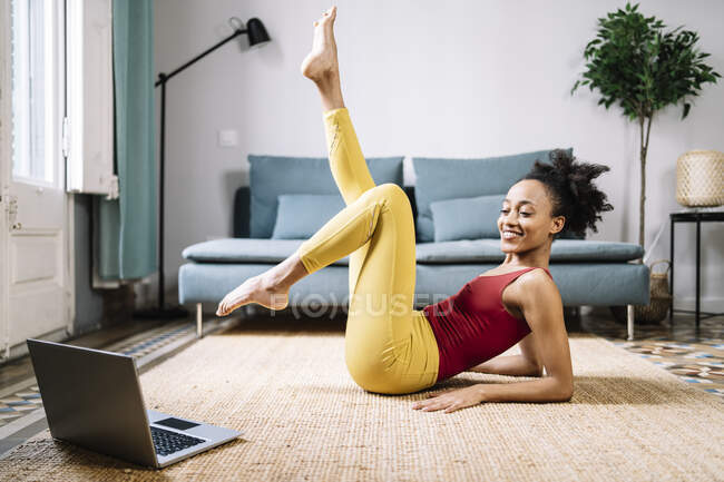 Lächelnde junge Frau beim Training, während sie zu Hause Tutorial auf dem Laptop anschaut — Stockfoto