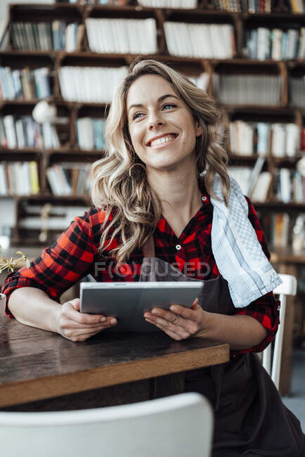 Femme souriante propriétaire avec tablette numérique regardant loin au café — Photo de stock