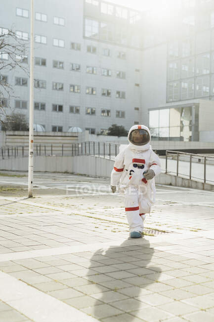 Joven astronauta en traje espacial caminando fuera del edificio durante el día soleado - foto de stock