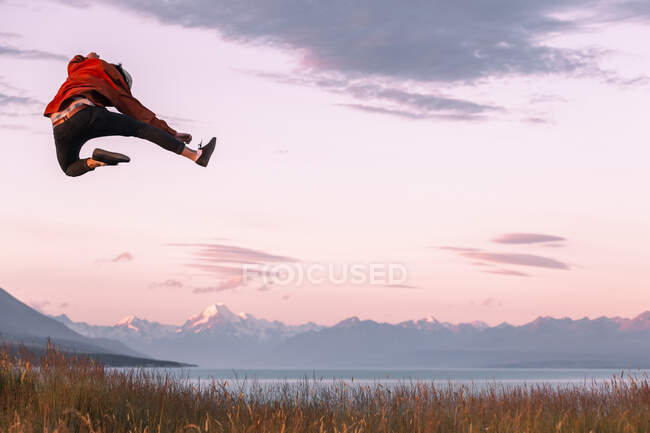 New Zealand, Canterbury, Rear view of young man jumping over Lake Pukaki at sunset — Stock Photo