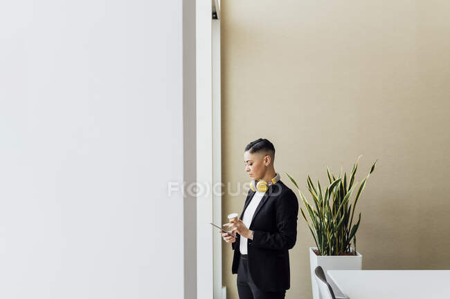 Female professional with disposable coffee cup using digital tablet in office — Stock Photo