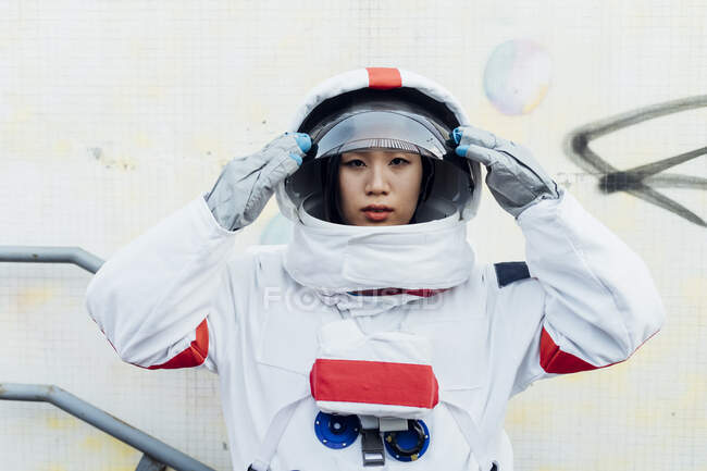 Female astronaut holding helmet while standing by wall — Stock Photo