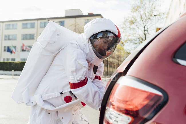 Astronauta en traje espacial abriendo baúl de coche en la ciudad — Stock Photo
