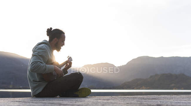 Giovane uomo che canta mentre suona ukulele sul lungomare durante la giornata di sole — Foto stock