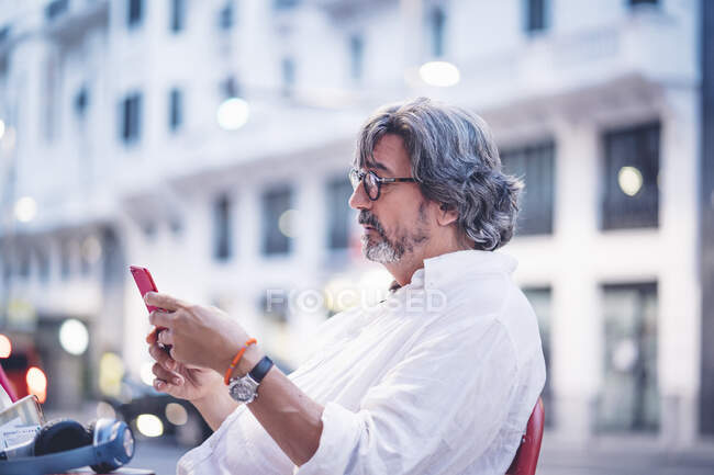 Homem sênior atraente usando telefone inteligente enquanto sentado no café da calçada em Madrid — Fotografia de Stock