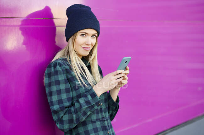 Smiling woman holding mobile phone while leaning on wall — Stock Photo