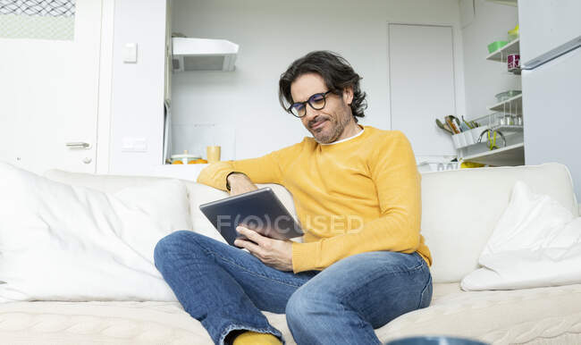 Людина з окулярами за допомогою цифрового планшету сидячи на дивані у вітальні. — стокове фото