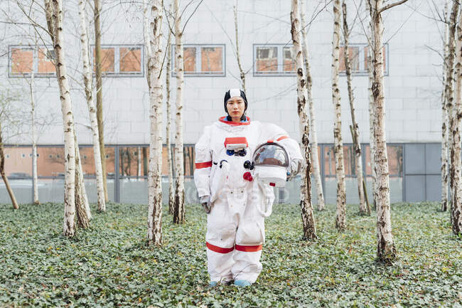 Astronauta hembra sosteniendo casco espacial mientras está de pie en el jardín - foto de stock