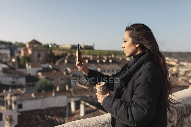 Mujer joven tomando selfie a través del teléfono móvil mientras está de pie en la azotea - foto de stock