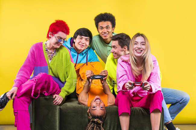 Glückliche Frauen spielen durch Gamepad, während sie mit Freunden vor gelbem Hintergrund sitzen — Stockfoto