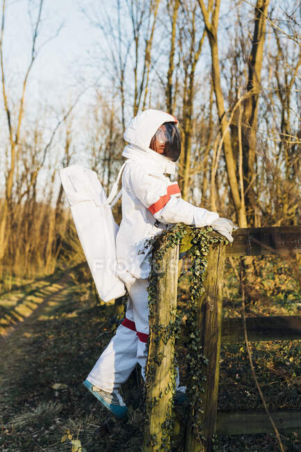 Young female astronaut in space suit and helmet standing by railing in forest - foto de stock