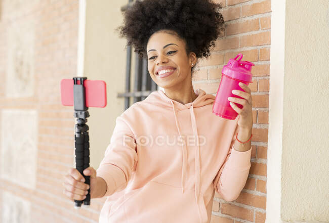 Cheerful woman with shaker vlogging while leaning on wall — Stock Photo