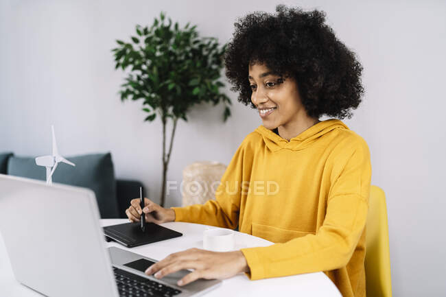 Mujer con tableta gráfica usando el ordenador portátil mientras está sentado en casa - foto de stock