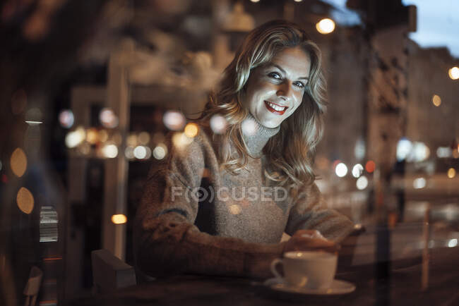 Donna sorridente con tablet digitale guardando attraverso la finestra del caffè — Foto stock