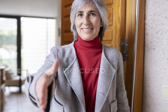 Smiling mature woman offering handshake at doorway — Stock Photo