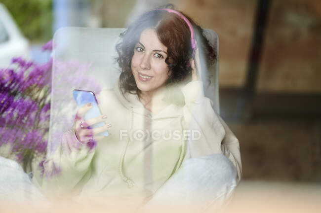 Усміхнена жінка з мобільним телефоном, який видно через вікно — стокове фото