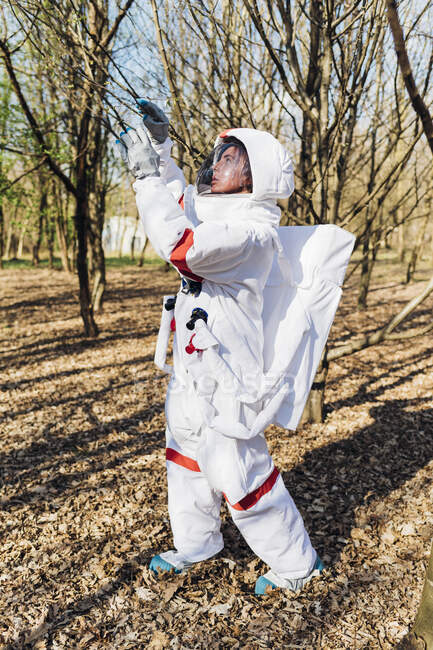 Young astronaut in space suit examining tree branch while exploring in forest — Stock Photo