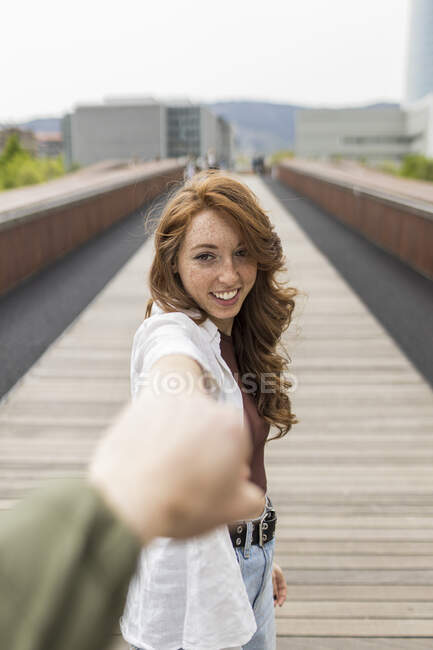 Дівчинка посміхається, тримаючи хлопця за руку на мосту — стокове фото