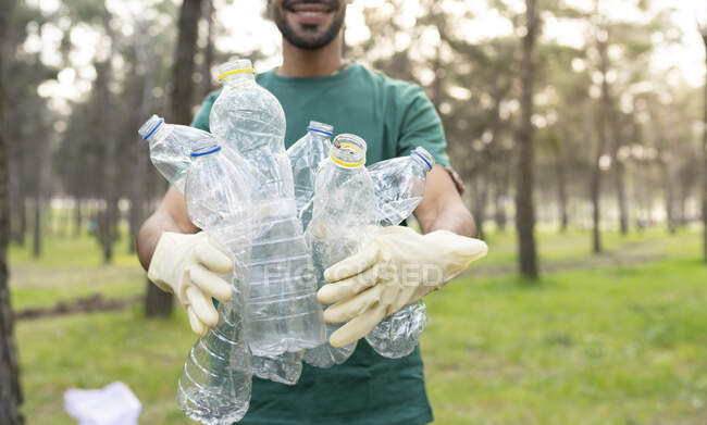 Мужчина-волонтер, держащий пластиковые бутылки во время уборки леса — стоковое фото