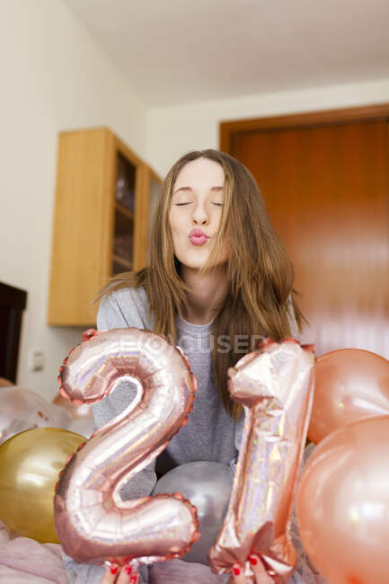Joven puckering mientras sostiene el número 21 globos en el dormitorio en casa - foto de stock