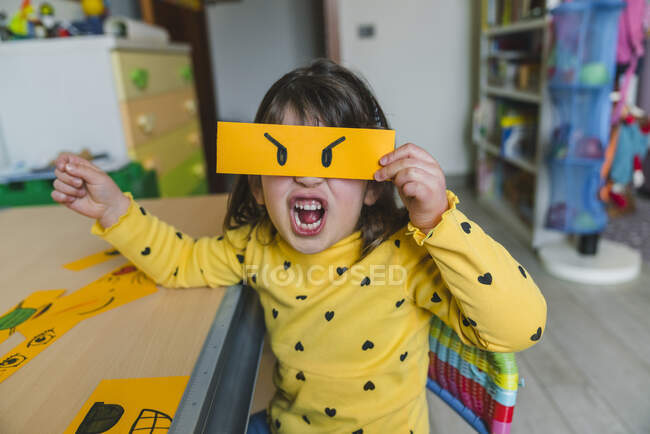 Girl making angry face while holding emoticon at home — Stock Photo