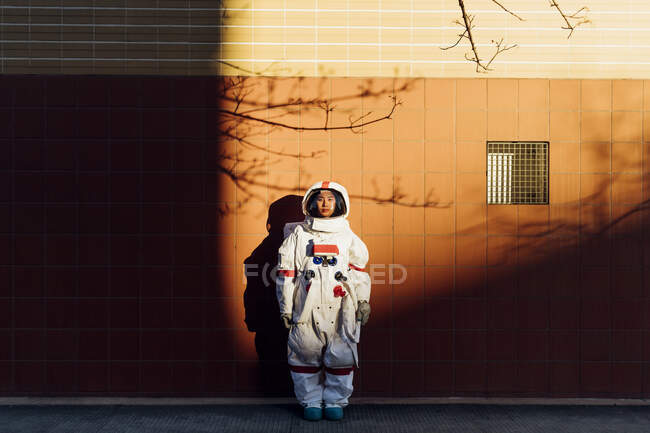 Mujer astronauta en traje espacial parada junto a la pared al atardecer - foto de stock