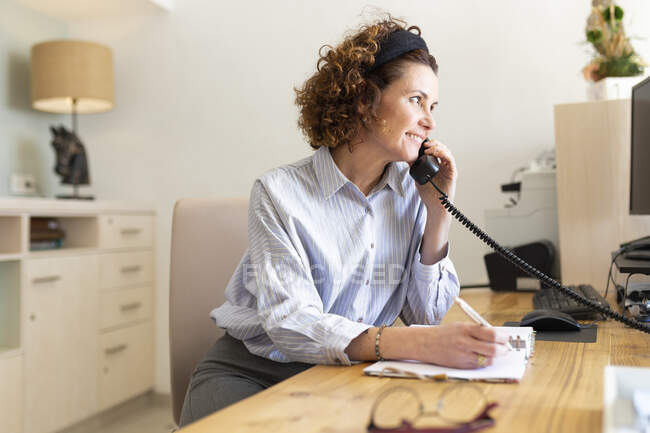 Female receptionist writing in dairy while talking on telephone at hotel — Stock Photo