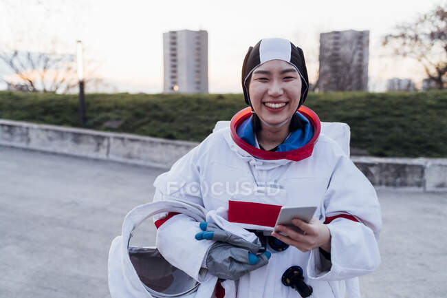 Mujer astronauta feliz con traje espacial sosteniendo el teléfono inteligente - foto de stock