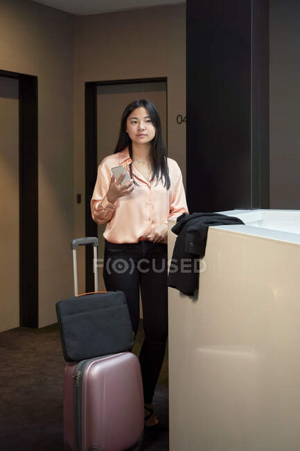 Mulher de negócios bonita olhando para longe enquanto segurando o telefone móvel no corredor do hotel — Fotografia de Stock