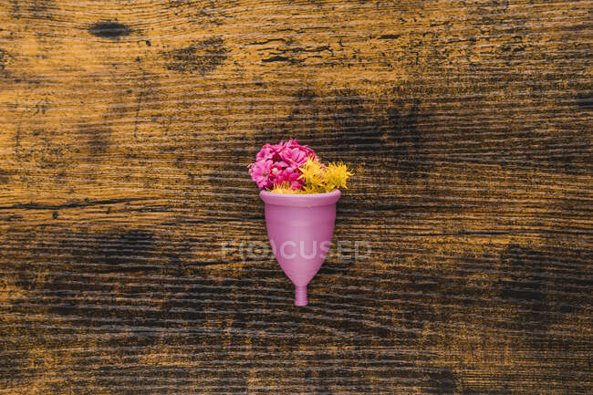Менструальная чашка с цветами на деревянном фоне — стоковое фото