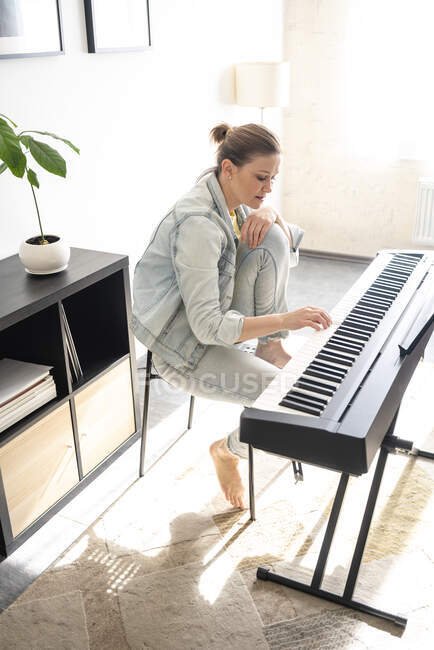 Femme adulte moyenne pratiquant le piano tout en étant assis dans le salon — Photo de stock