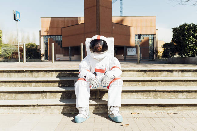 Homem astronauta de terno espacial sentado em degraus durante o dia ensolarado — Fotografia de Stock