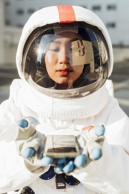 Astronauta en traje espacial mirando el teléfono inteligente en las manos durante el día soleado - foto de stock