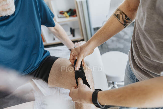 Чоловік фізіотерапевт наклеює еластичну терапевтичну стрічку на коліно пацієнта. — стокове фото