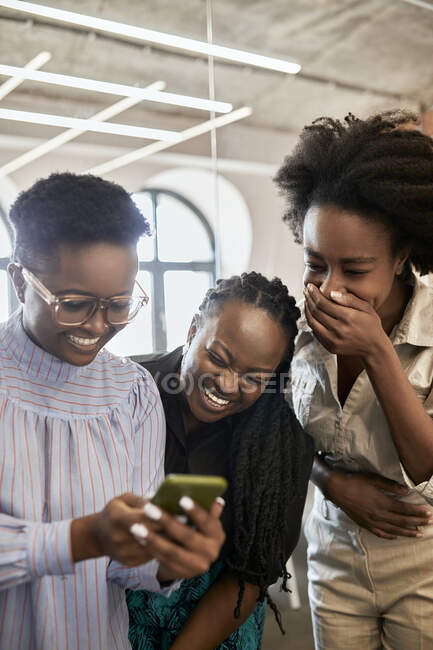 Felice professionista femminile utilizzando il telefono cellulare da colleghi di lavoro femminili ridere di coworking office — Foto stock