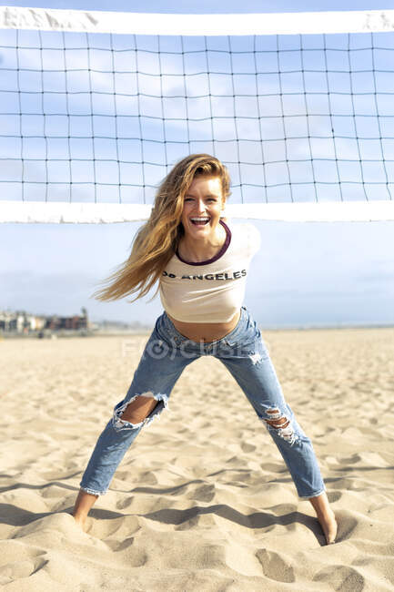 Грайлива молода жінка нахиляється на волейбол сіті на пляжі в сонячний день. — стокове фото