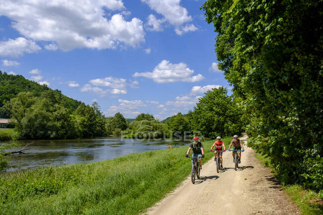 Німеччина, Баварія, Дуггендорф, Троє зрілих дорослих їдуть на велосипеді вздовж річки Нааб. — стокове фото
