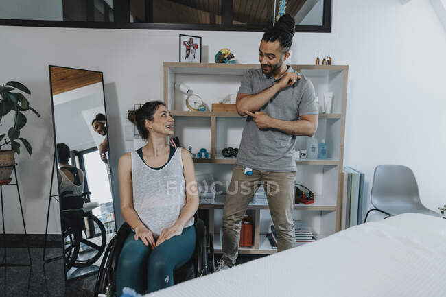 Smiling male physiotherapist pointing at elbow while explaining patient in medical practice — Photo de stock